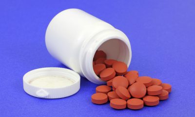 A white pill bottle with generic ibuprofen pain pills on a blue background.